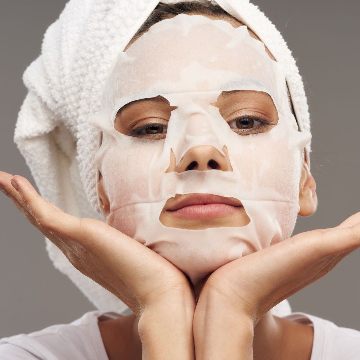 Gezichtsmasker op het gezicht van een vrouw. Vrouw met handdoek. Masker bedekt gezicht. Ogen, neus, mond zichtbaar. Handen onder kin.