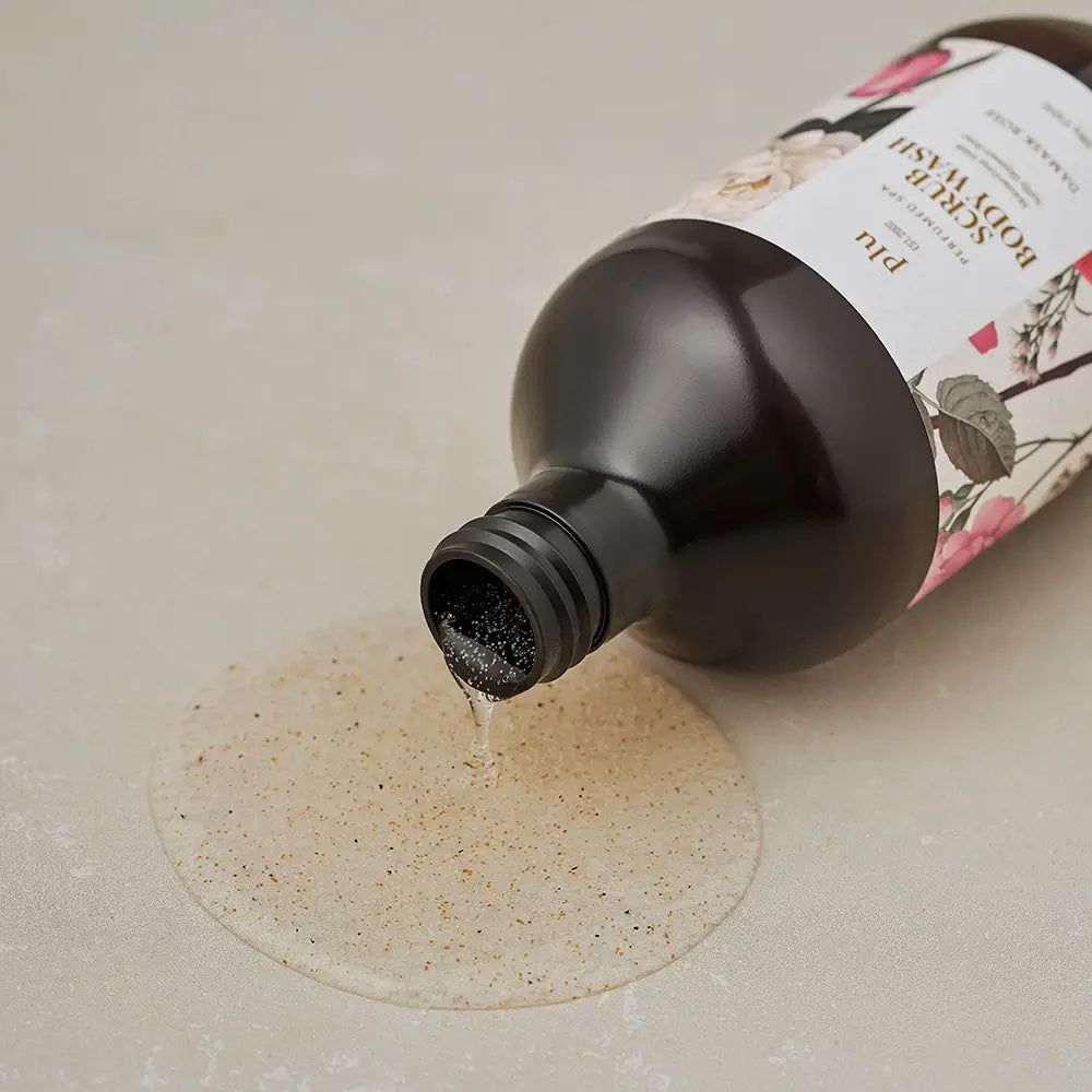 PLU Scrub Body Wash Damask Rose wordt uit een bruine fles op een oppervlak gegoten.