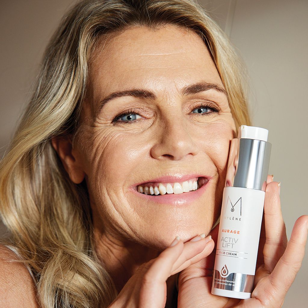 Femme tenant un tube de crème. Inscription: MYLÈNE, AURAGE ACTIV LIFT, FACE CREAM. Bouchon argenté, tube blanc.