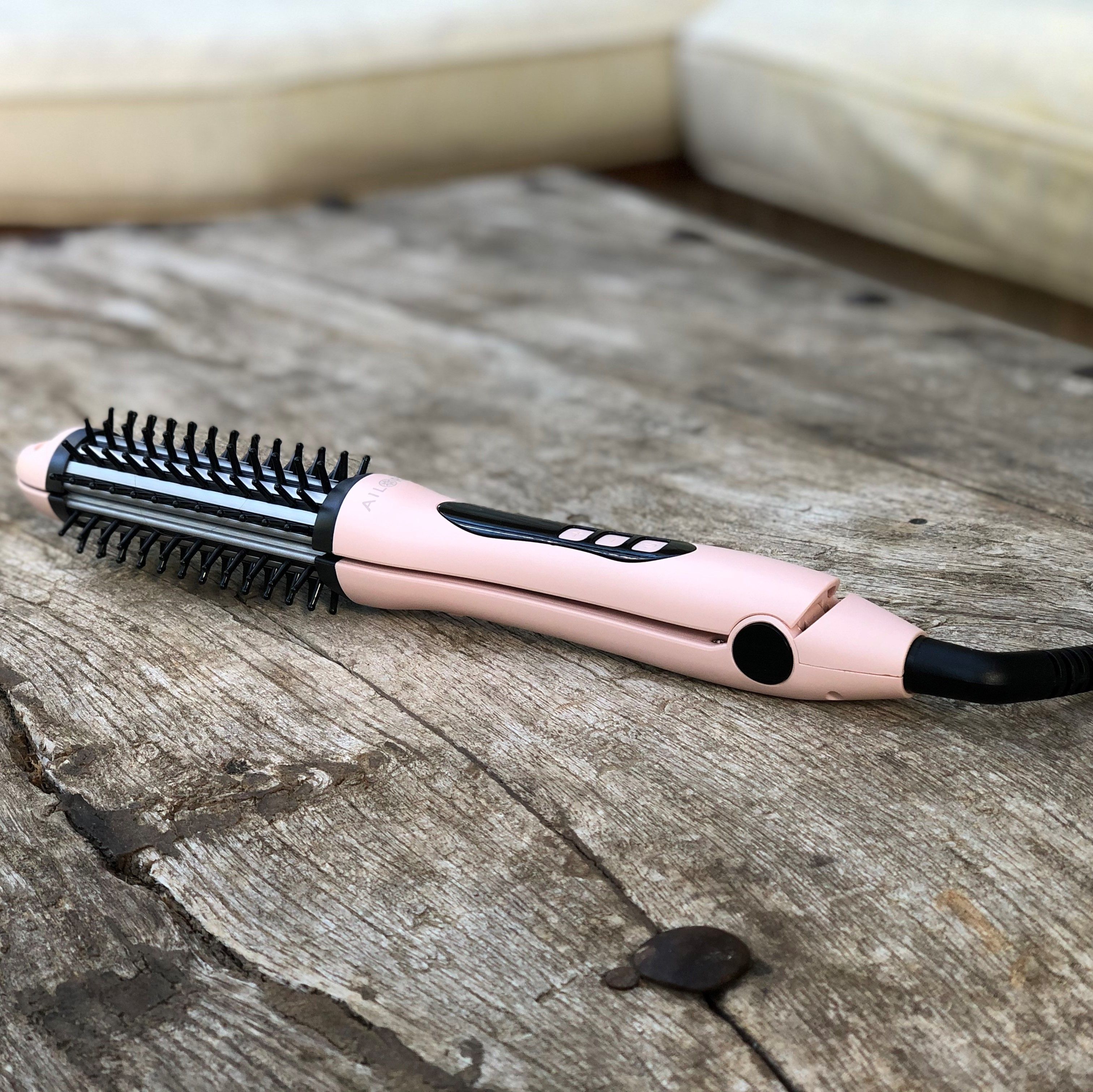 Roze stijltang op houten oppervlak. Zwarte borstelkop, digitale display. Zwarte kabel.