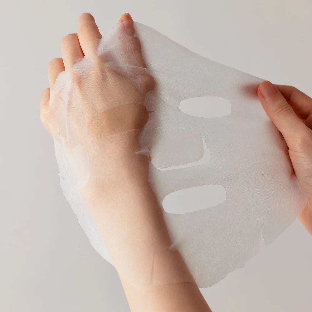 Handen houden een transparant gezichtsmasker vast. Het masker heeft openingen voor ogen, neus en mond.