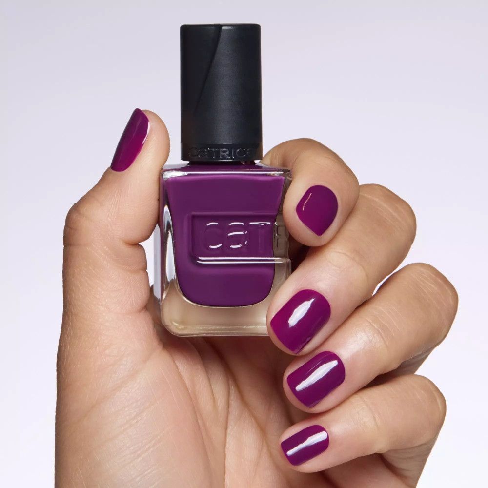Main avec ongles vernis. Vernis à ongles violet foncé. Flacon avec bouchon noir. Sur fond clair.