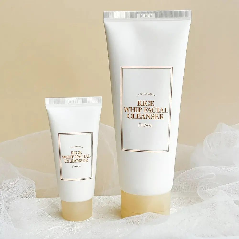 Deux tubes "Rice Whip Facial Cleanser" de différentes tailles. Les deux avec des étiquettes marron et des inscriptions. Sur tissu blanc.