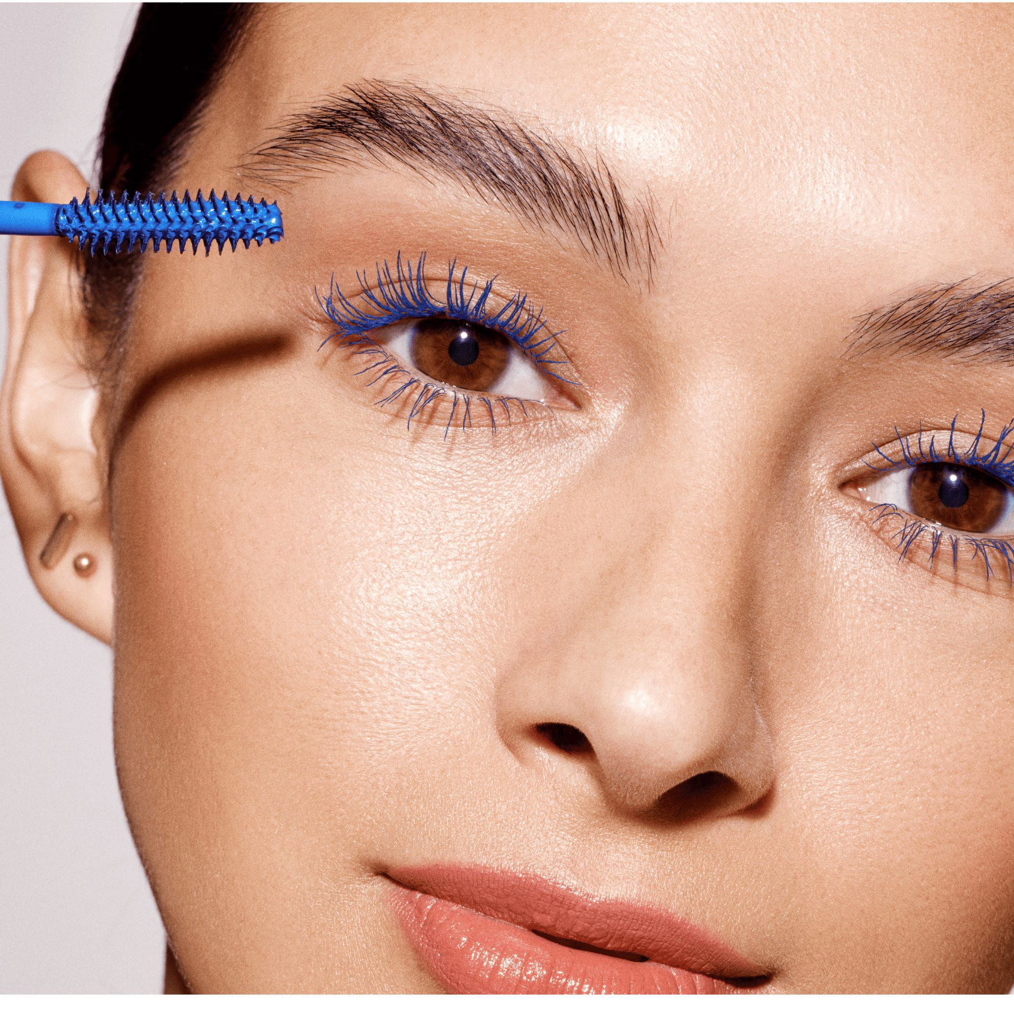 Une femme applique du mascara bleu avec la brosse bleue du Double-Ended Volume Set.