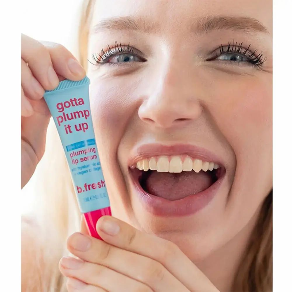 Vrouw houdt een lichtblauwe en roze tube "gotta plump it up" voor haar mond. Merk: b.fresh.