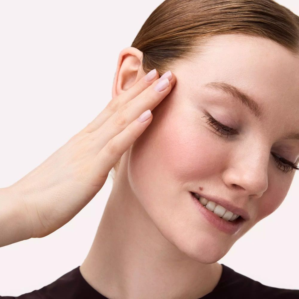 Vrouw raakt zachtjes haar wang aan. Blush op de wangen. Gesloten ogen.