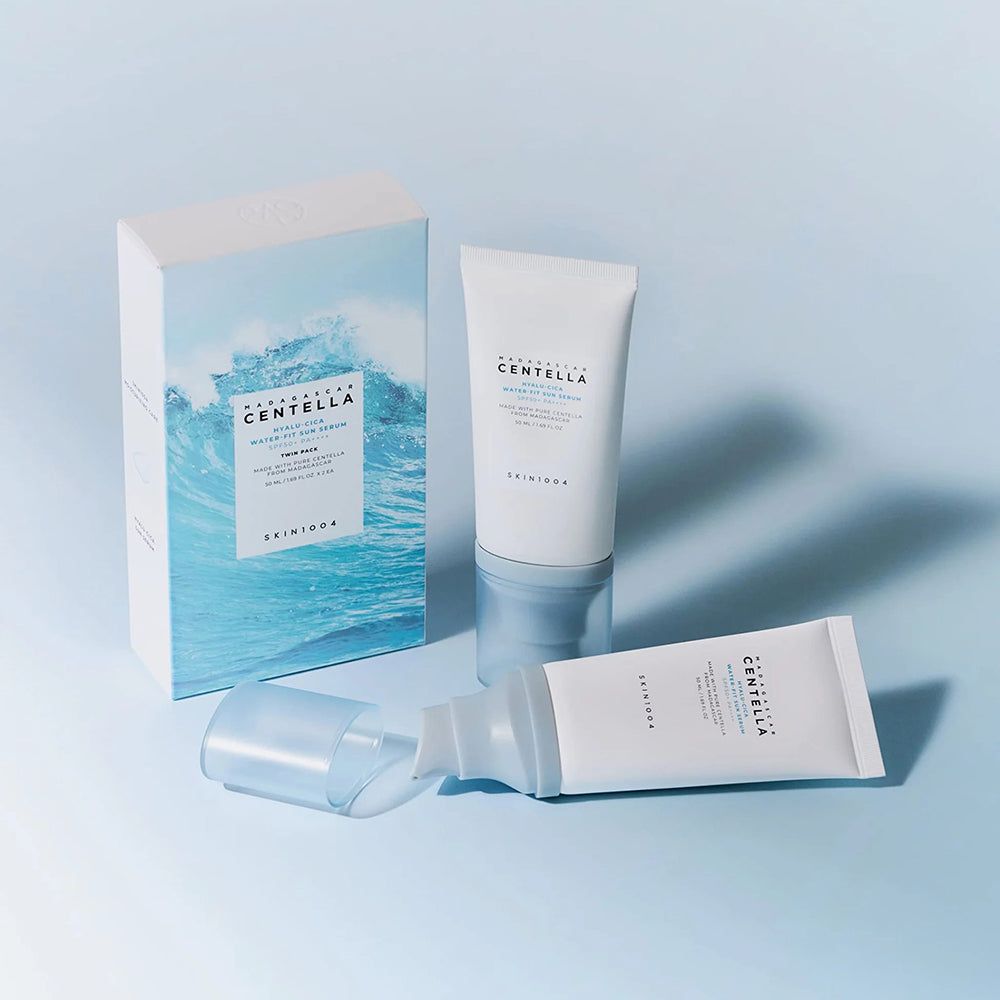 Deux tubes de crème solaire et un emballage à motif de vagues. Un tube est couché. Texte: SKIN1004, Hyalu-Cica Water-Fit Sun Serum SPF50+.