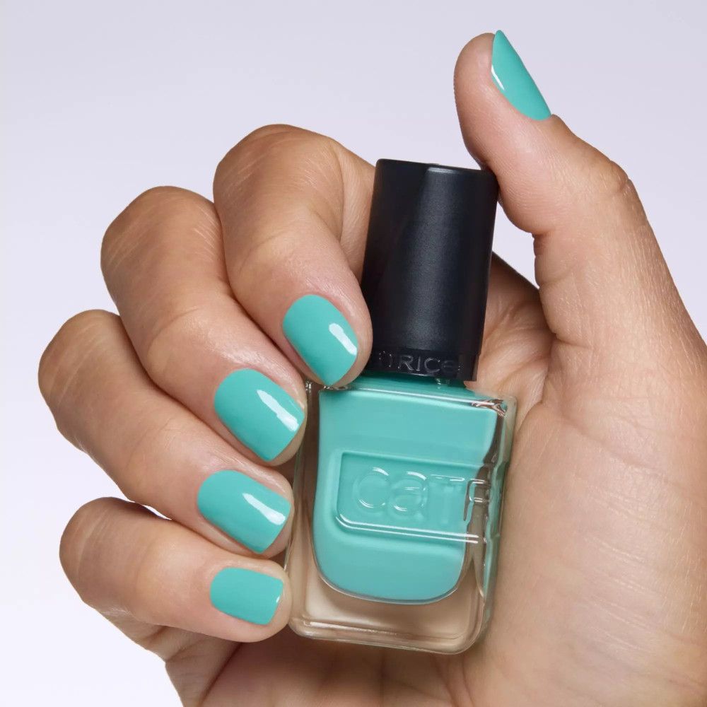 Une main tient un flacon de vernis à ongles turquoise. Les ongles sont vernis avec le même vernis.