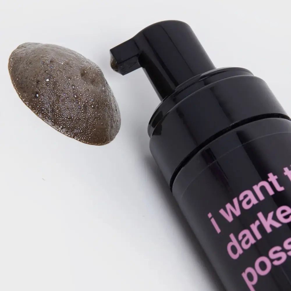 Flacon noir avec pompe et échantillon de mousse bronzante. Inscription "I want the darkest tan possible".