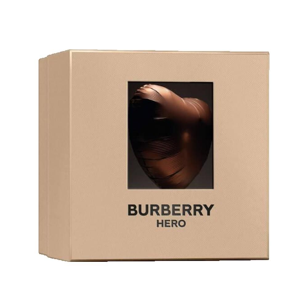 Emballage beige avec fenêtre carrée. Sculpture en bronze en forme de cœur visible à travers la fenêtre. "Burberry Hero" en dessous.