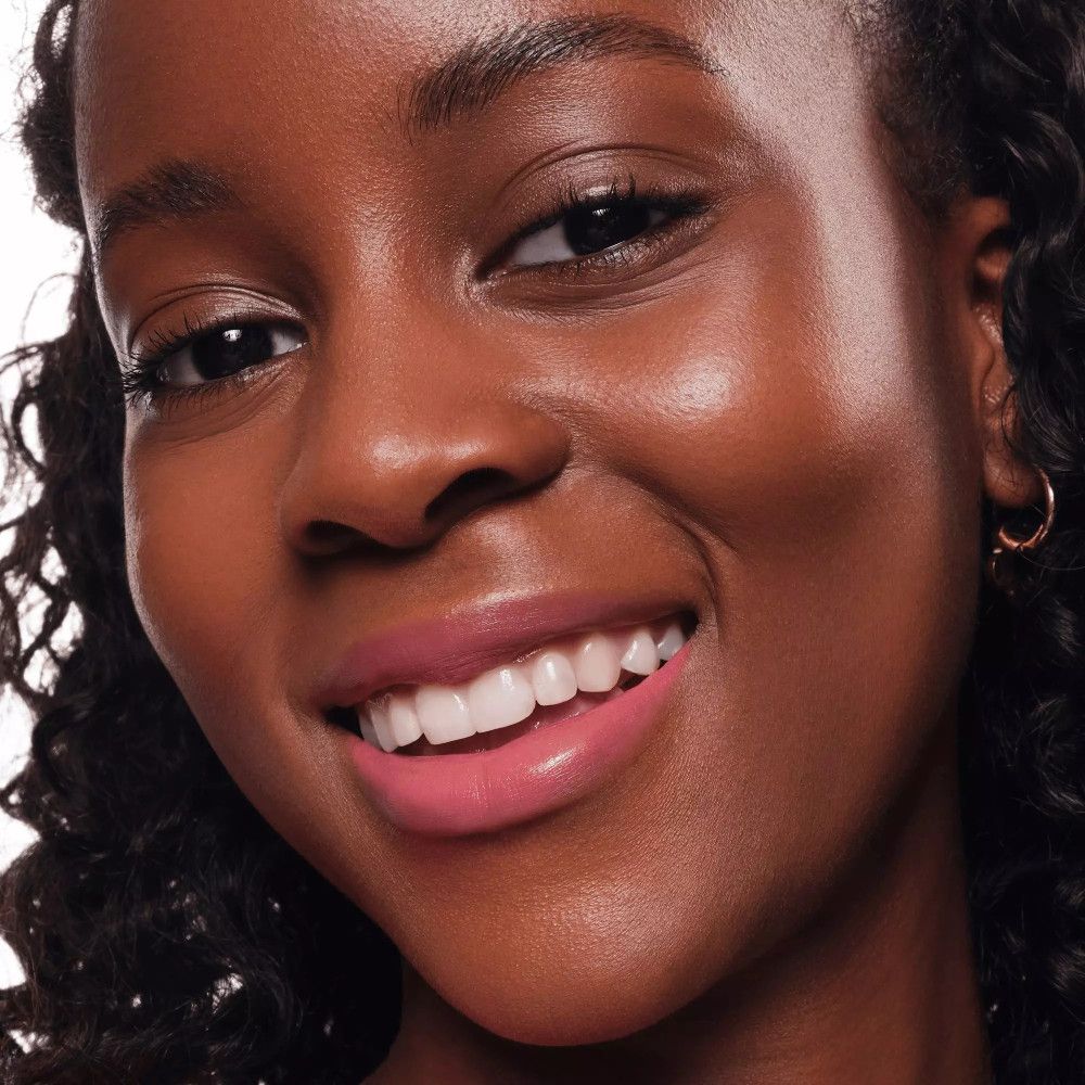 Portrait d'une femme à la peau foncée avec des lèvres roses. Elle sourit.