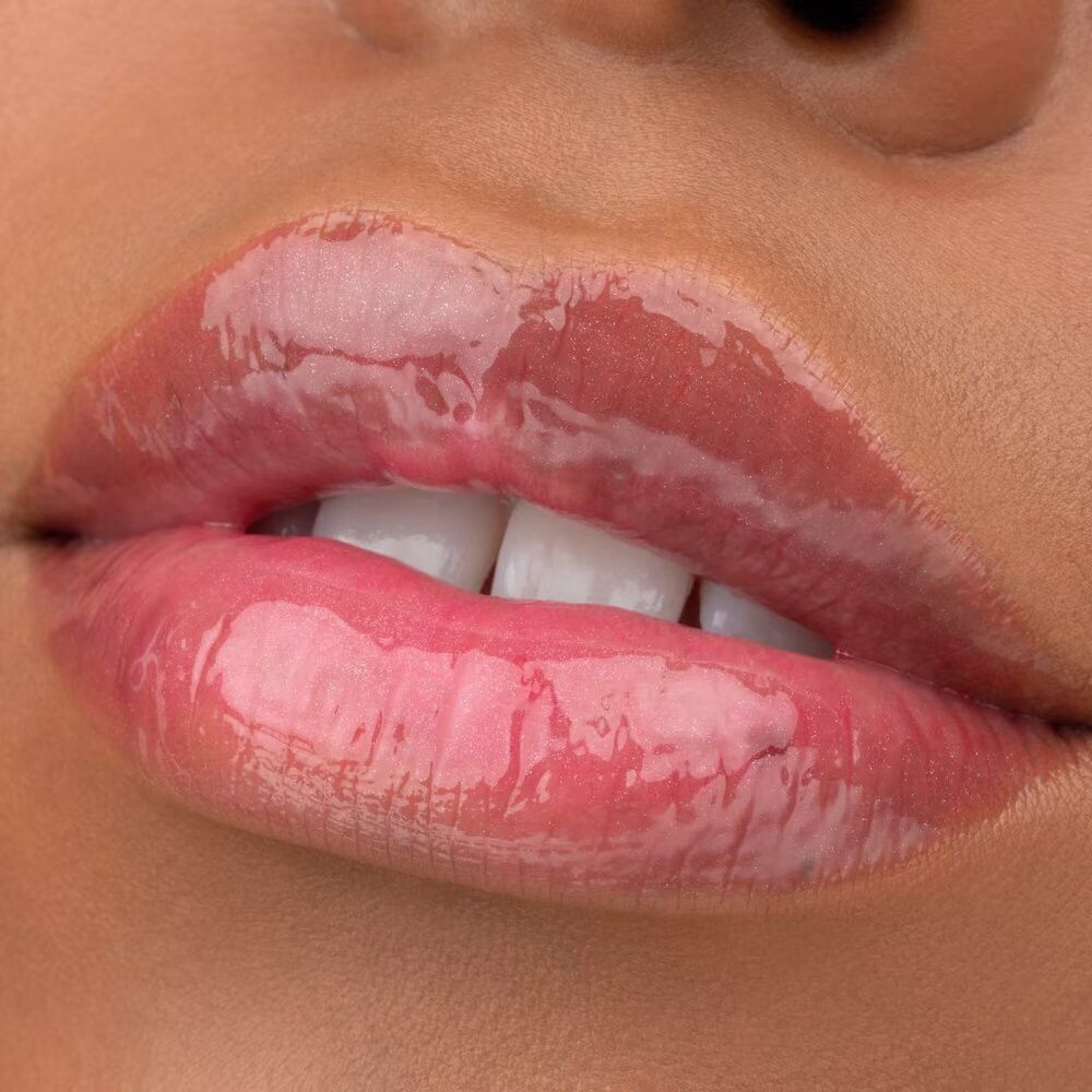 Gros plan sur des lèvres avec un gloss rose brillant. Dents blanches visibles.
