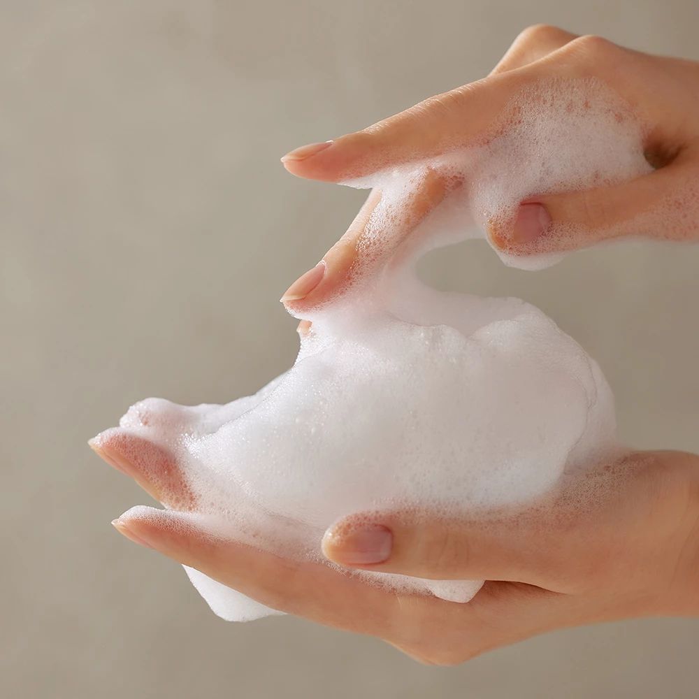 Mains avec mousse blanche. La mousse est tenue entre les doigts.