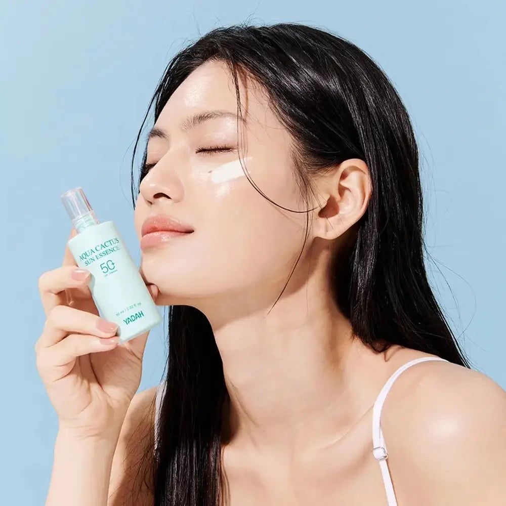 Vrouw met gesloten ogen houdt een flesje vast. Product aangebracht op de huid. Flesje met de tekst YADAH Aqua Cactus Sun.