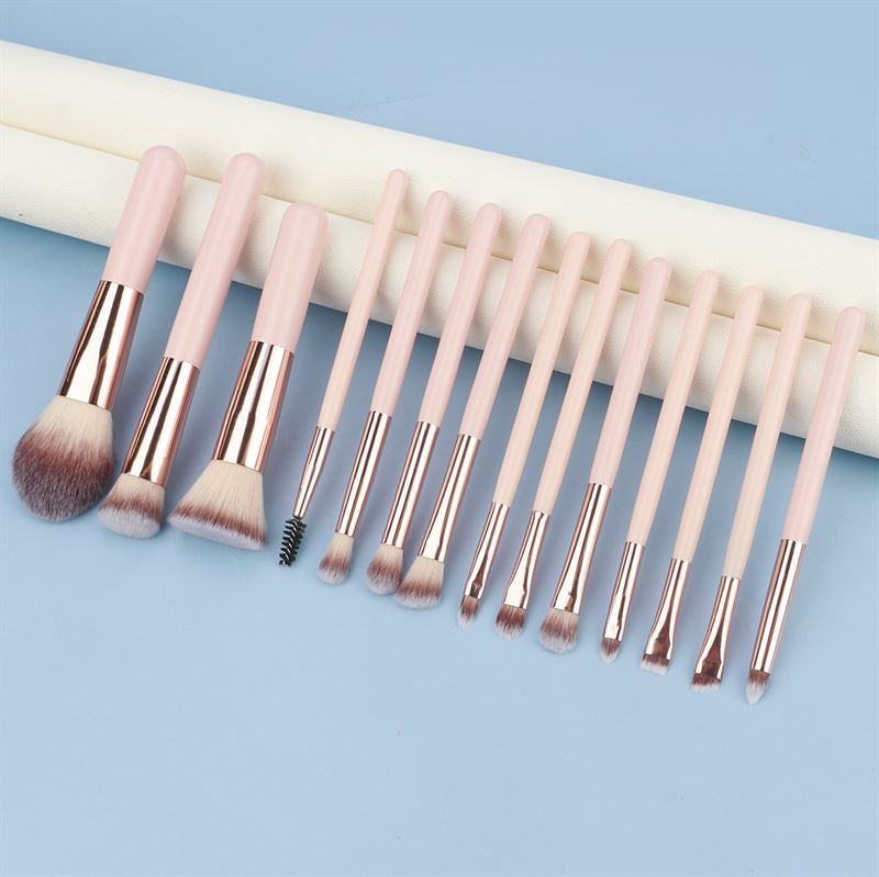 Ensemble de pinceaux de maquillage. Manches roses, viroles dorées, différentes têtes. Sur fond bleu.