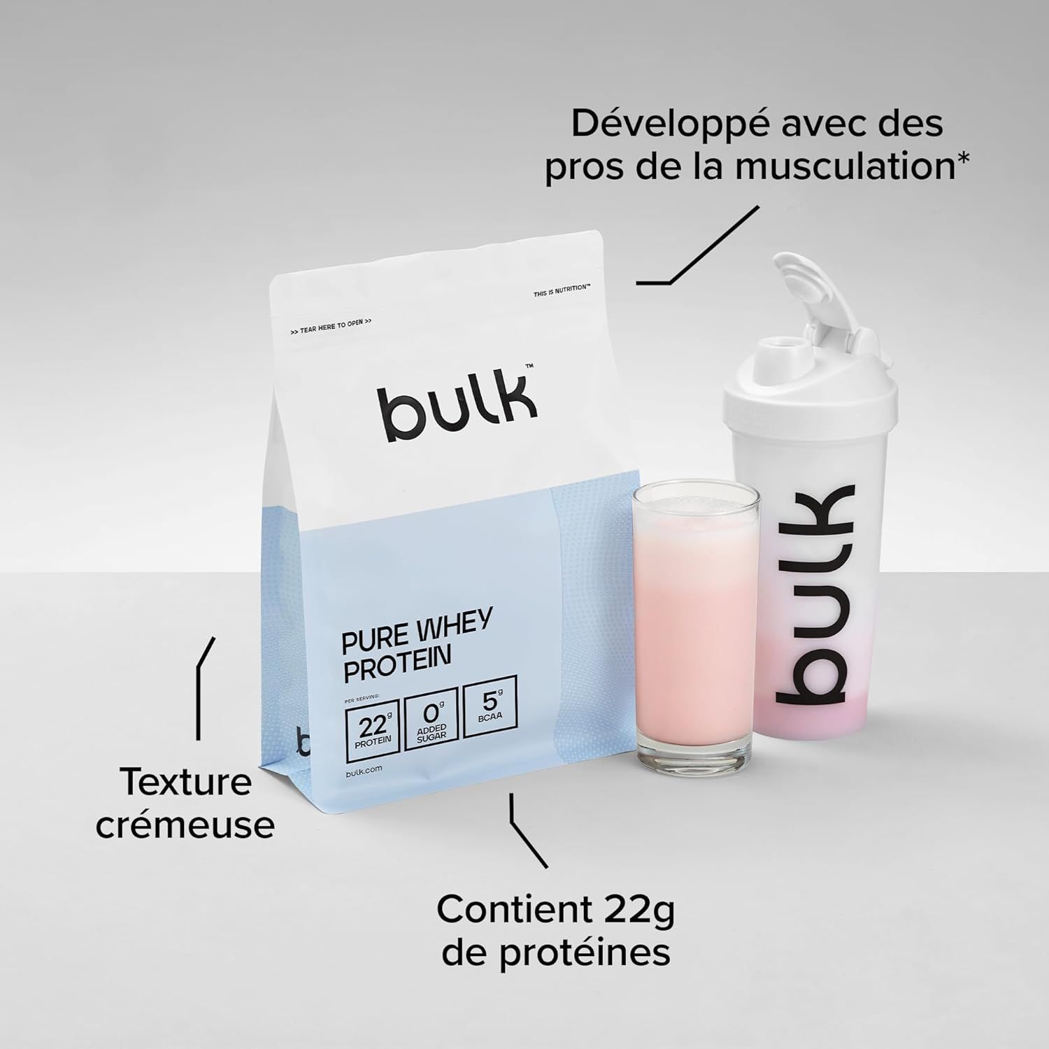 Sachet "Pure Whey Protein" de Bulk, un verre de shake protéiné rose et un shaker blanc.