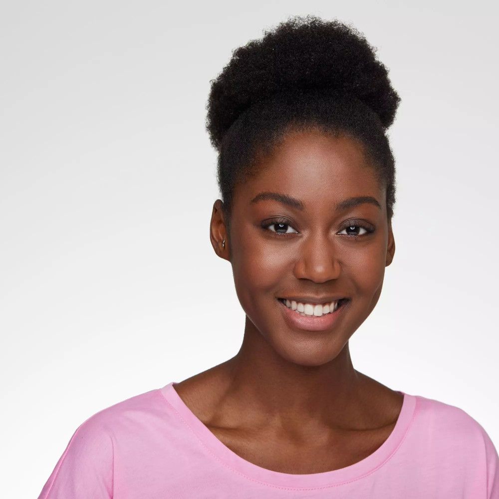 Portrait d'une femme souriante à la peau foncée et aux cheveux relevés. Elle porte un t-shirt rose.