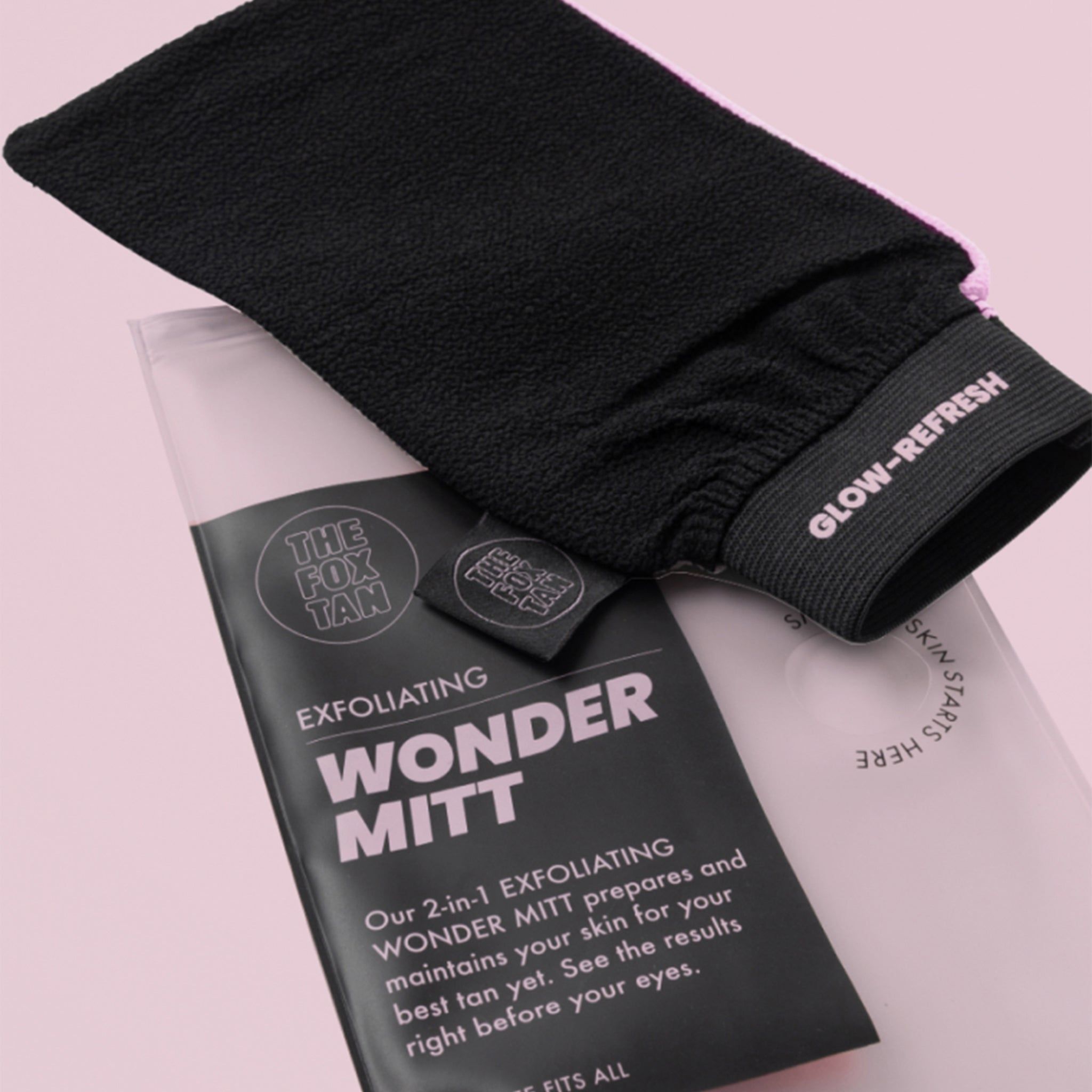 Gant exfoliant noir et emballage avec informations sur le produit. Fond rose.