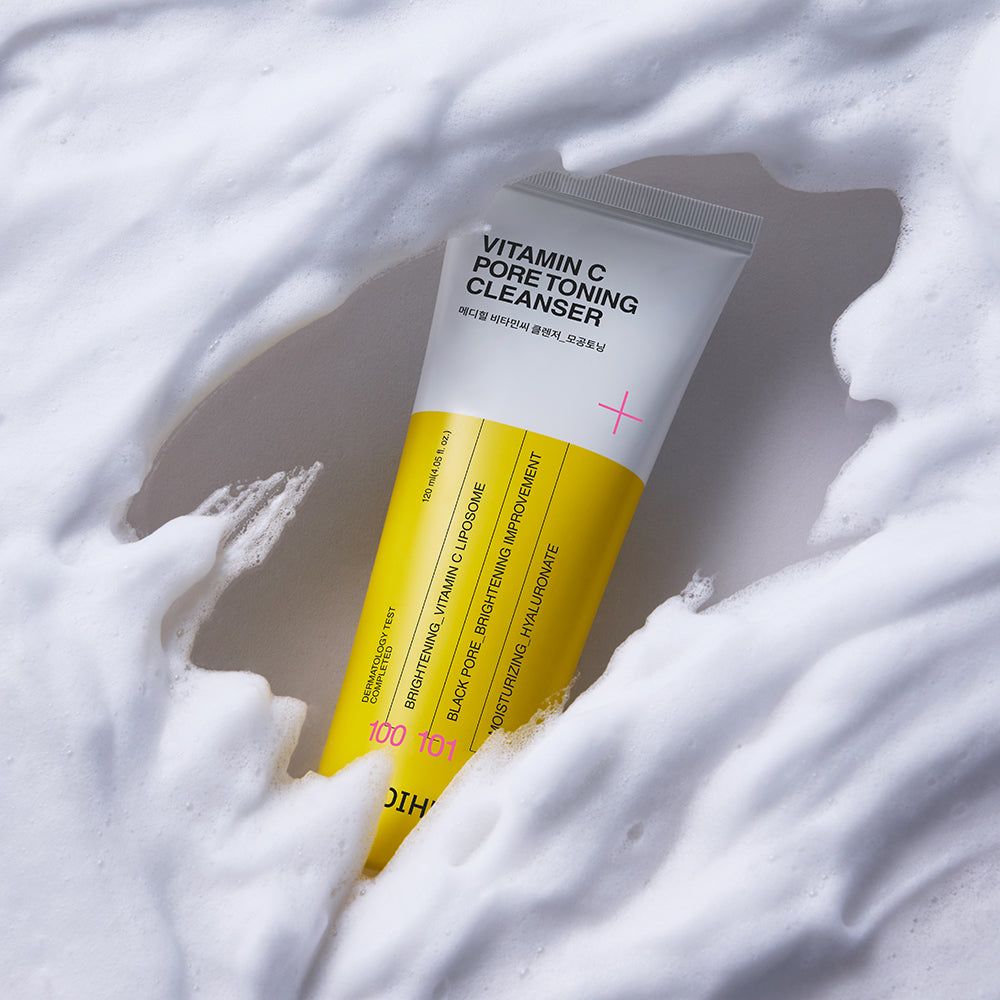 Gele tube in witte schuim. Opschrift: Vitamin C Pore Toning Cleanser. Roze plus-teken. Gele strook met tekst.