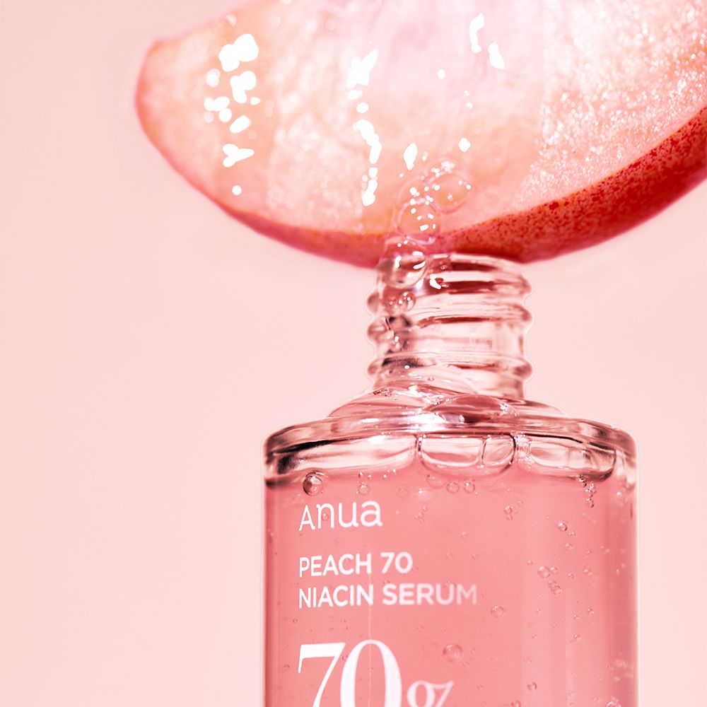 Druppels van een perzikschijf vallen in de Anua Peach 70 Niacin serumfles.