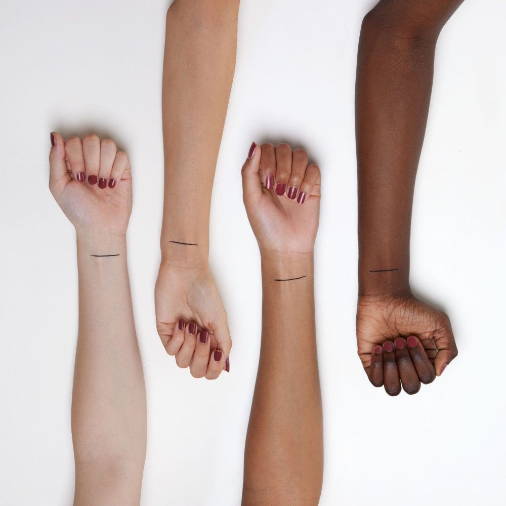 Quatre bras de différentes couleurs de peau. Un trait d'eye-liner noir sur chaque bras.