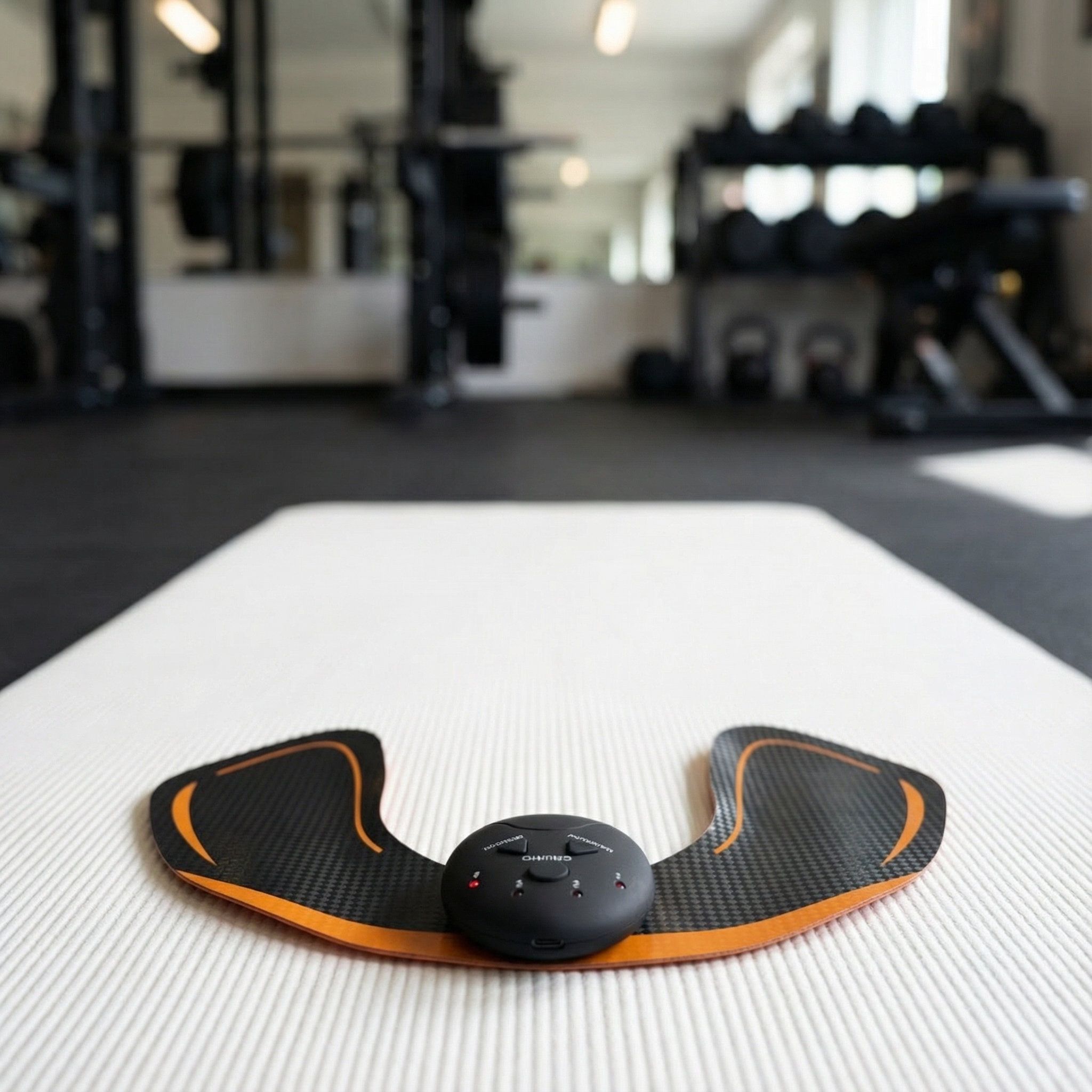 Stimulateur EMS fessier avec unité de contrôle et deux électrodes ailes sur un tapis de fitness.