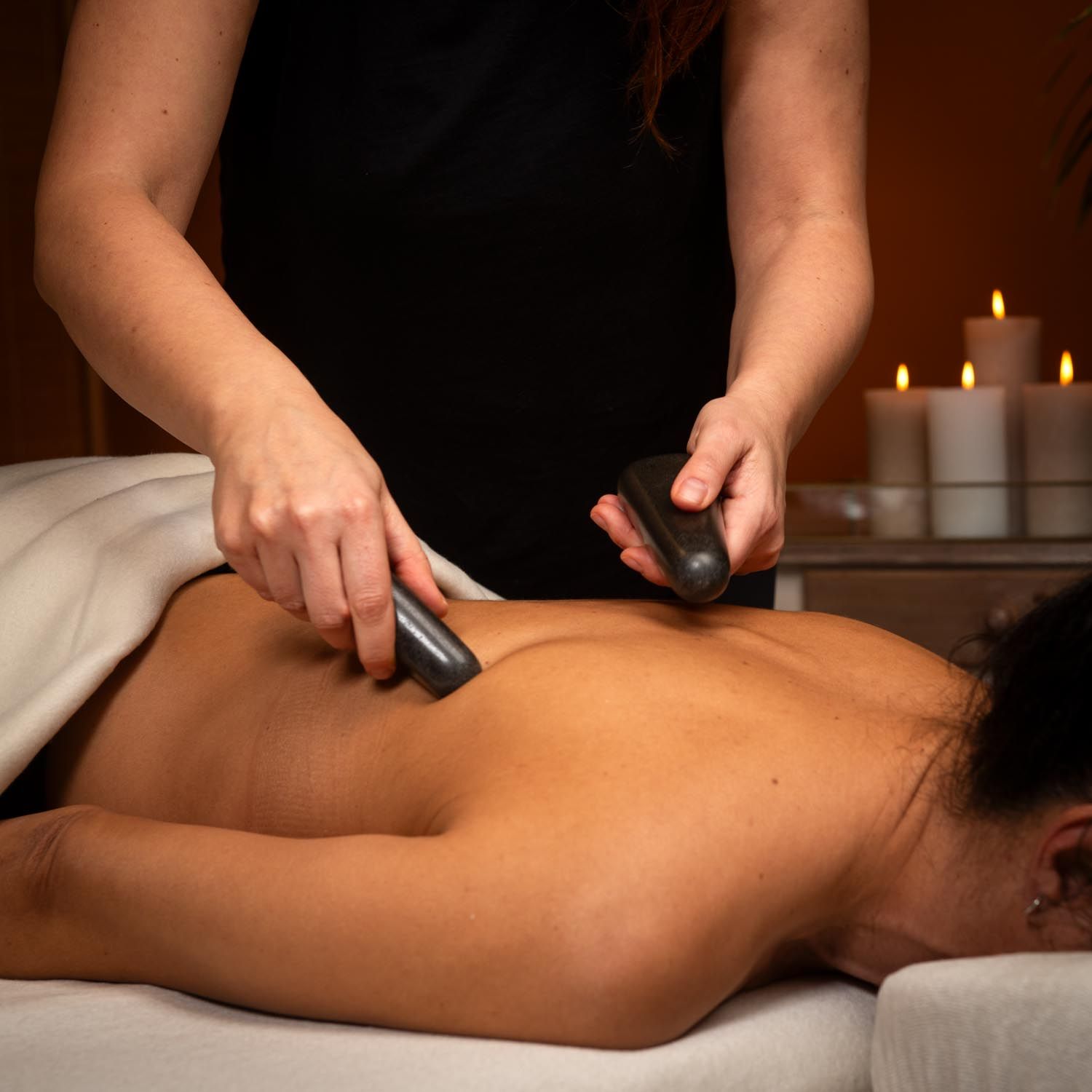 Persoon houdt twee donkere, langwerpige stenen op de rug van een persoon. Kaarsen op de achtergrond.