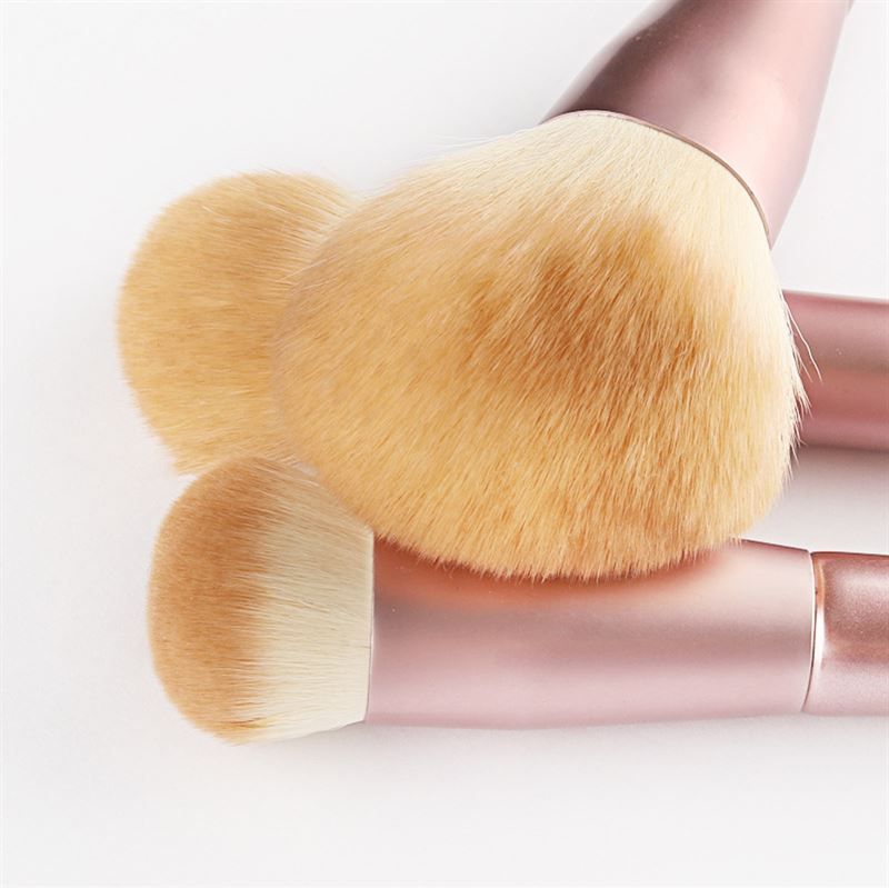 Close-up van drie make-up kwasten. Roze handvatten, lichte borstelharen. Verschillende vormen. Op witte achtergrond.