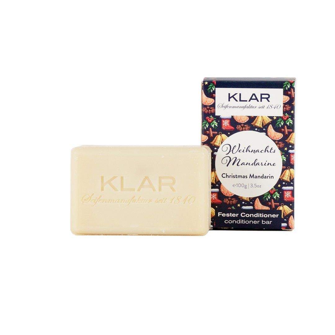 Barre revitalisante Klar-Seifen rectangulaire, crème, à côté de l'emballage. Emballage avec décor de mandarine et de Noël. Texte : "Fester Conditioner".