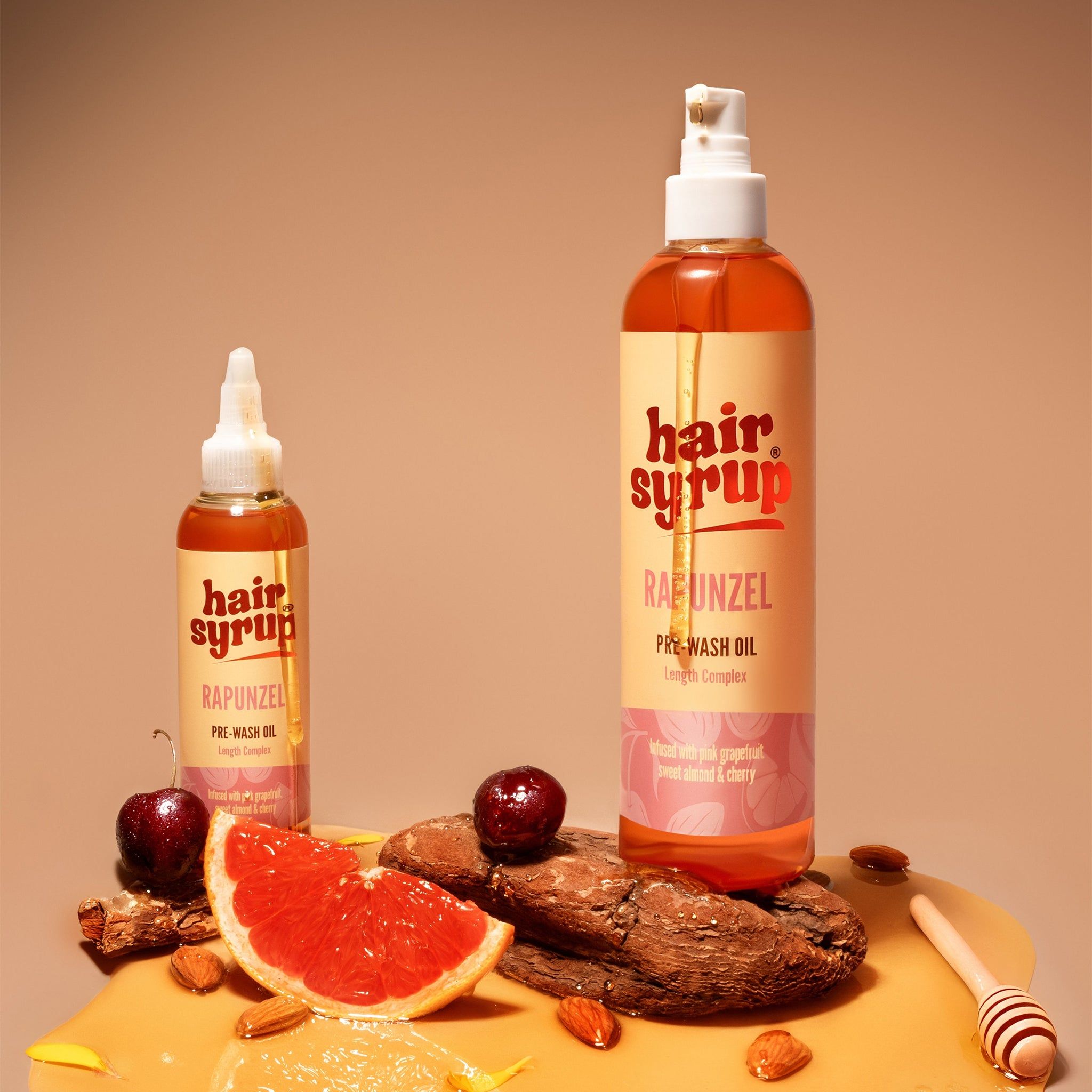 Twee Hair Syrup flessen, Rapunzel Pre-Wash Oil, naast grapefruit, honing en amandelen op hout.
