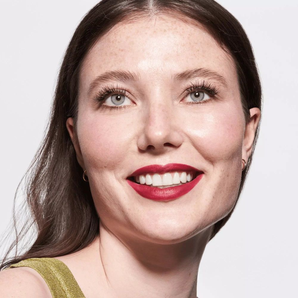 Portrait d'une femme avec de faux cils appliqués et du rouge à lèvres rouge. Elle sourit.