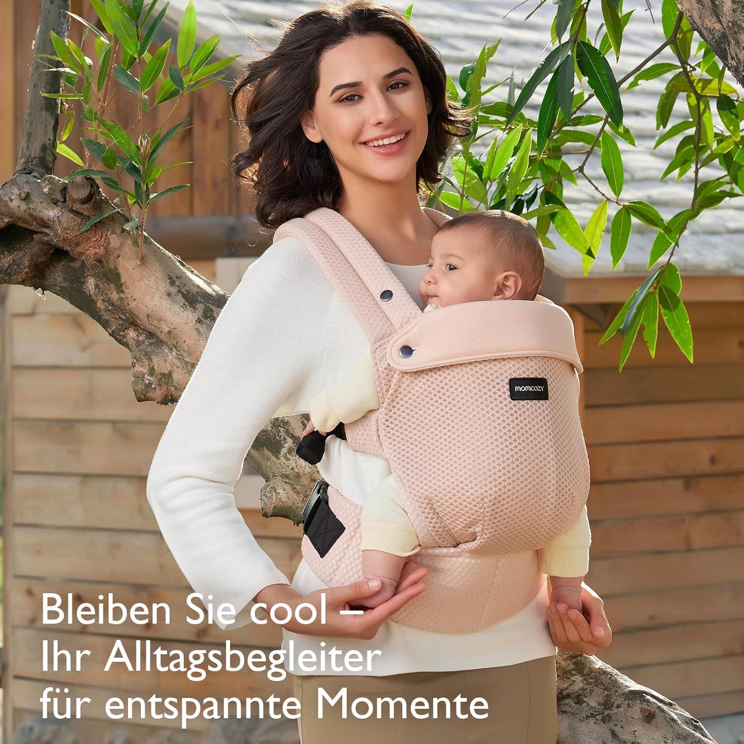 Roze babydrager met baby buiten, gedragen door een vrouw.