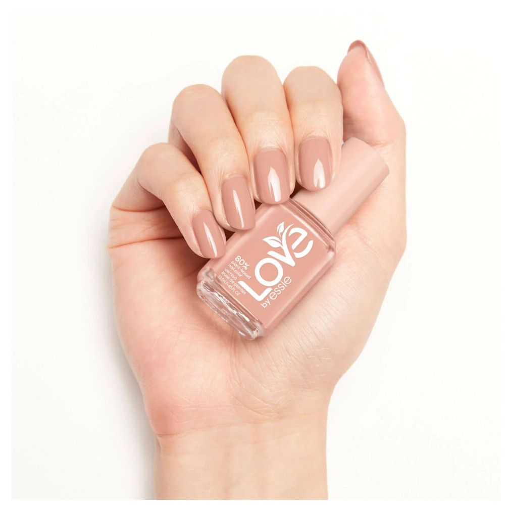 Hand met gelakte nagels en nagellakfles. Fles met logo 'Love by Essie'.