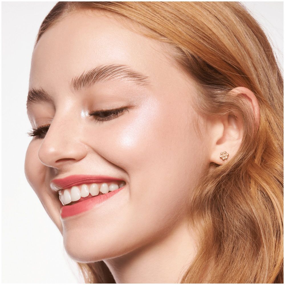 Gros plan d'un visage souriant. Peau uniforme et éclatante. Boucles d'oreilles dorées.