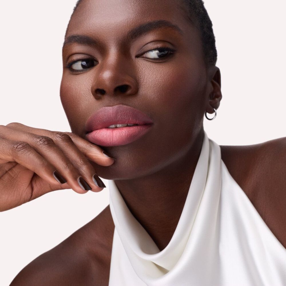 Portrait d'une femme avec du rouge à lèvres rose. Elle porte un haut blanc et des boucles d'oreilles.