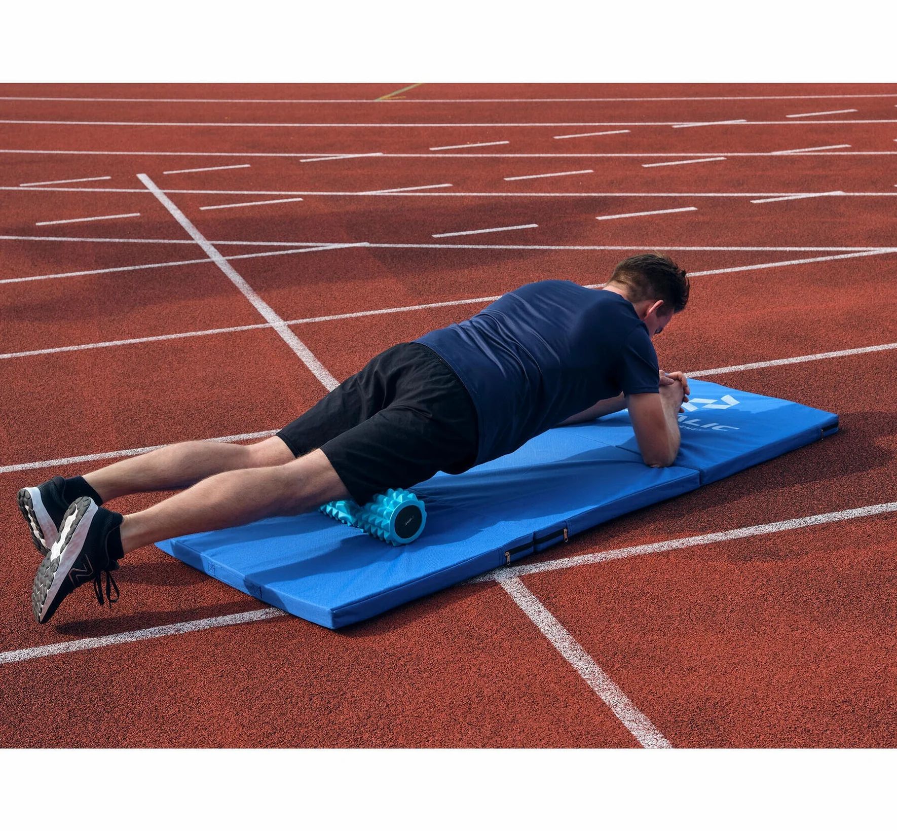 Persoon op blauw gymnastiekmat met foamroller. Op rode atletiekbaan. Logo zichtbaar.
