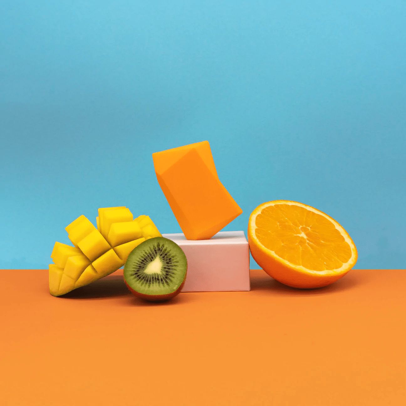 Blocs oranges, mangue, kiwi et moitié d'orange. Sur fond orange et bleu.