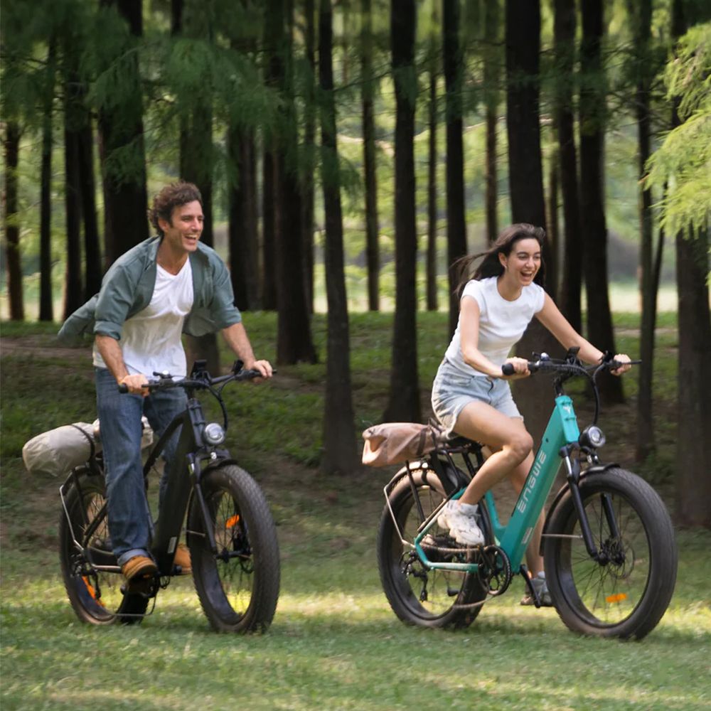 Twee personen rijden op elektrische mountainbikes op een gazon. Beide fietsen hebben brede banden.