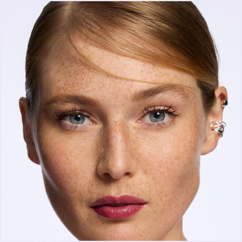 Portrait d'une femme avec des taches de rousseur. Rouge à lèvres appliqué. Aucune information sur le produit visible.