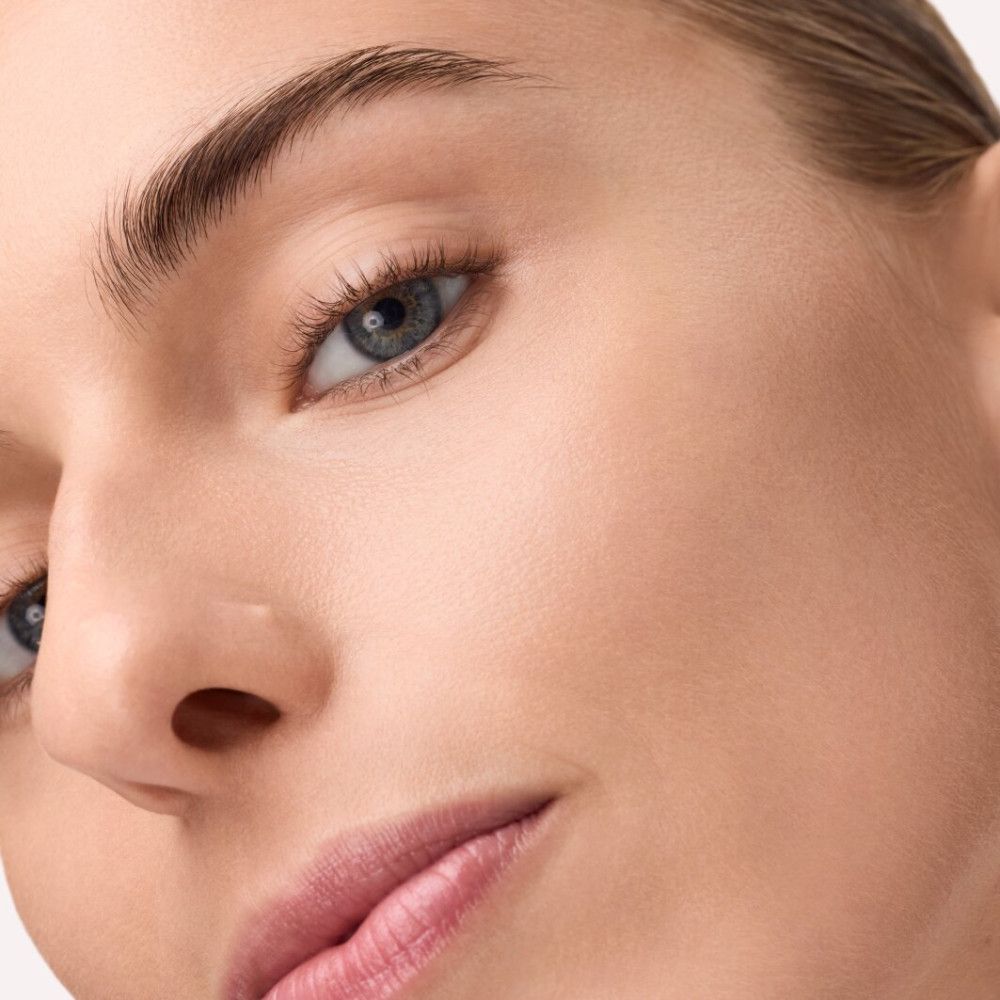 Close-up van een gezicht. Huid ziet er egaal en verzorgd uit. Blauwe ogen, volle lippen.