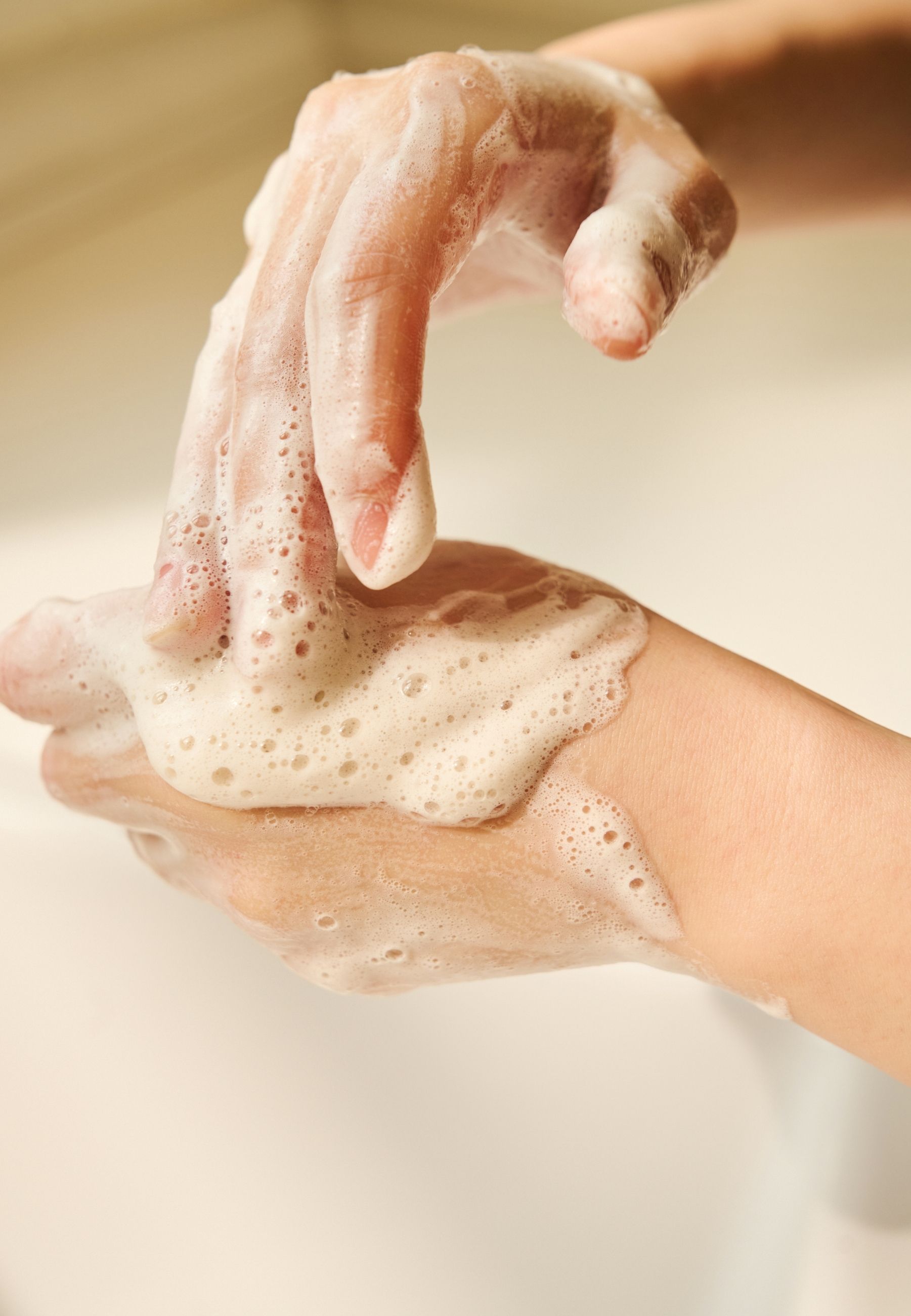 Handen bedekt met schuim. Schuim is wit en romig. Handen in de buurt van een wastafel.