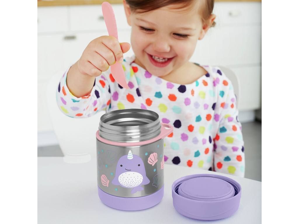 Kind houdt roze lepel boven open roestvrijstalen thermosfles met narwal-motief. Paars deksel ernaast. Tafel met eten.