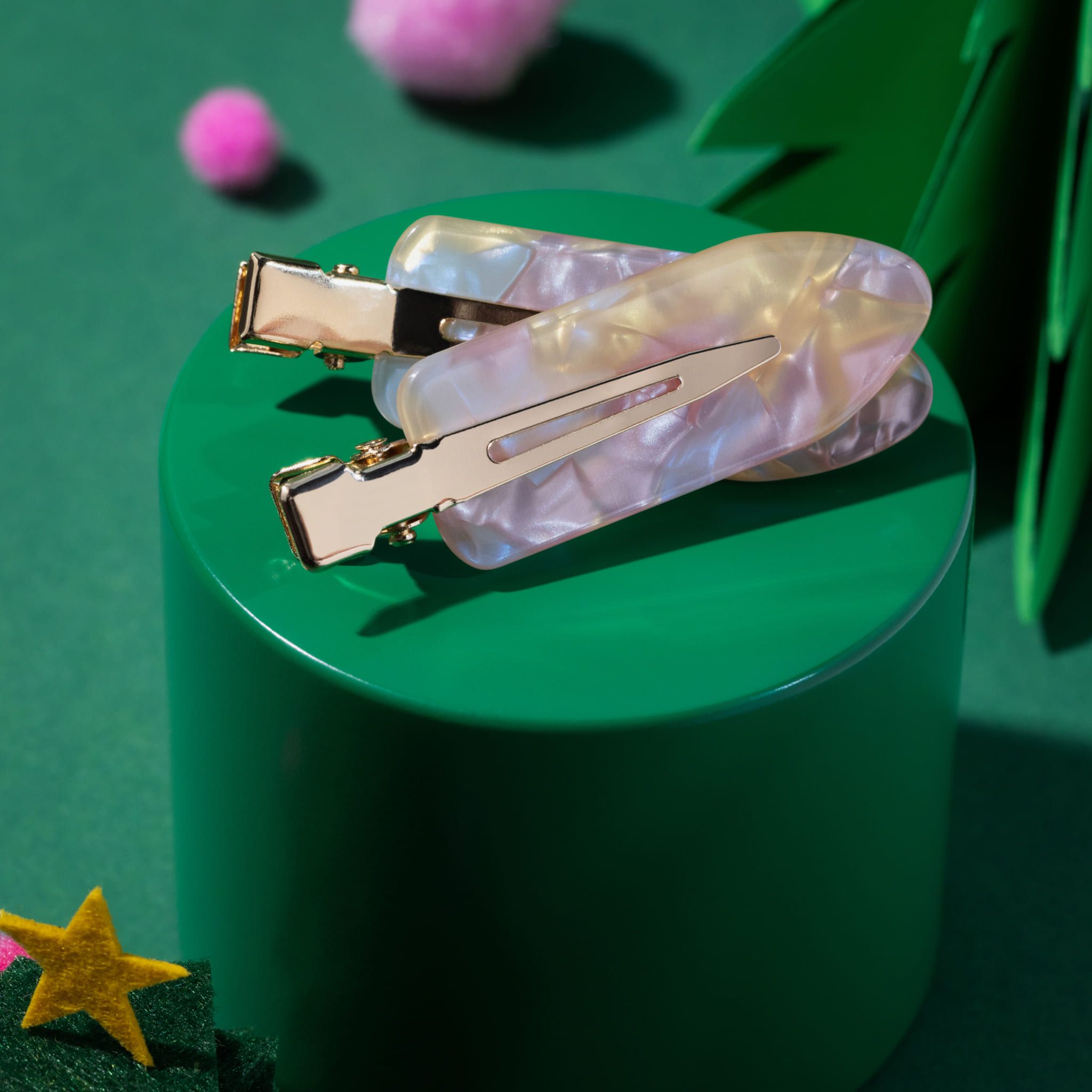 Deux pinces à cheveux avec détails dorés. Sur un piédestal vert.