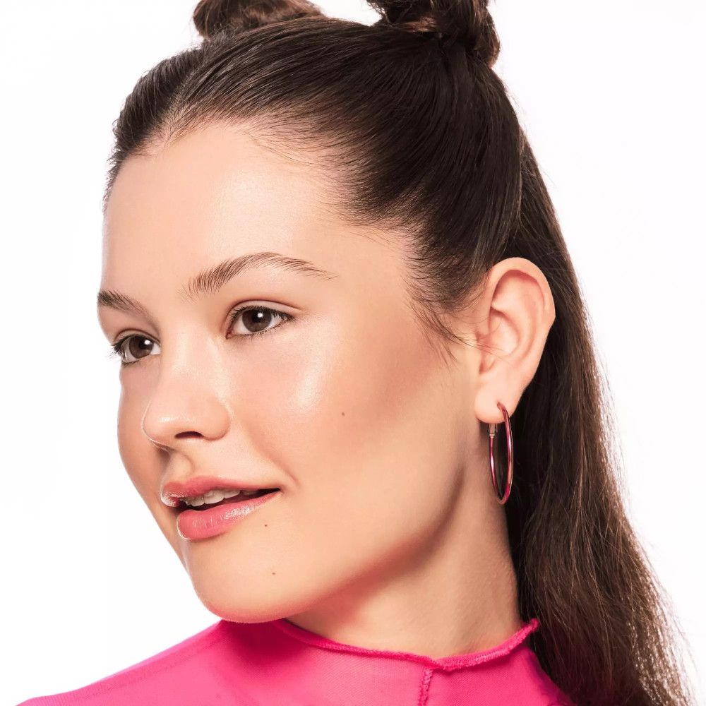 Portret van een vrouw met roze oorbellen en huid waarop bronzer is aangebracht.