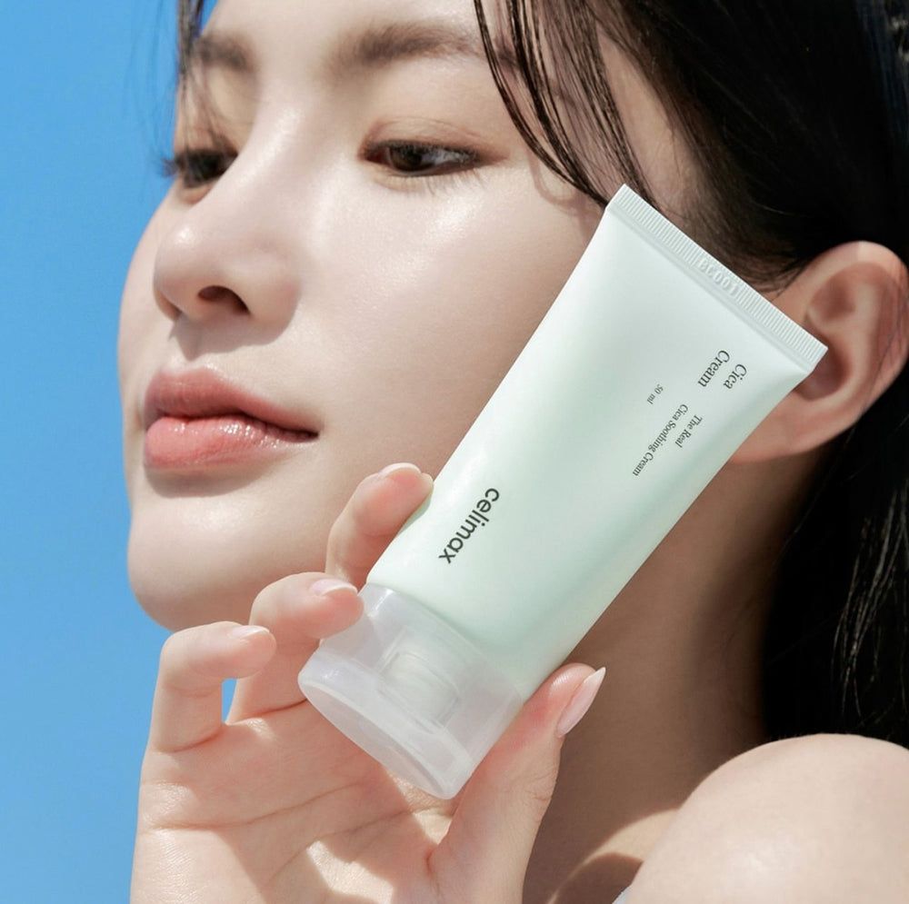 Vrouw houdt Celimax Cica Creme tube vast voor blauwe lucht.