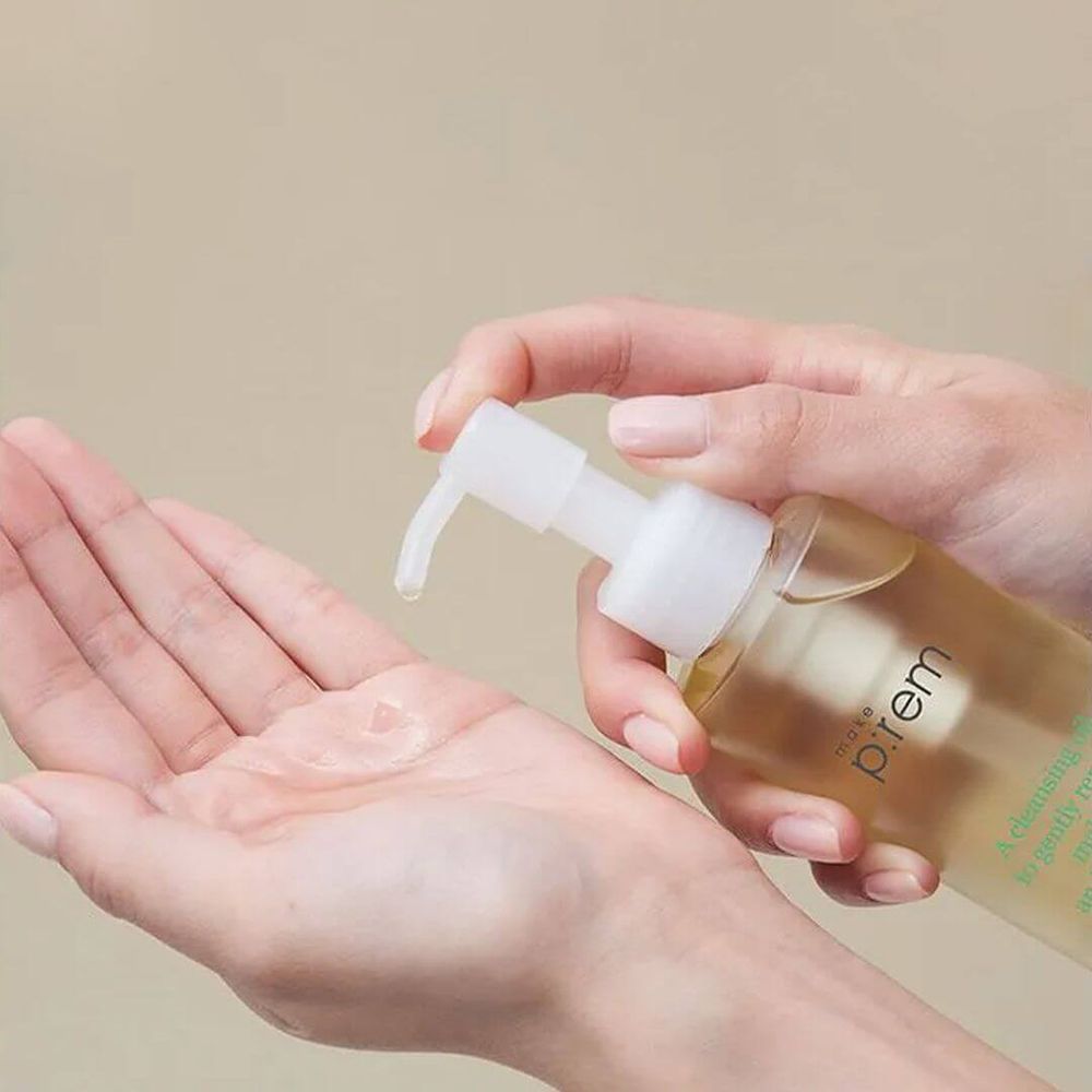 Handen houden een fles reinigingsolie vast. De pomp geeft olie in de handpalm. Het product is zichtbaar.