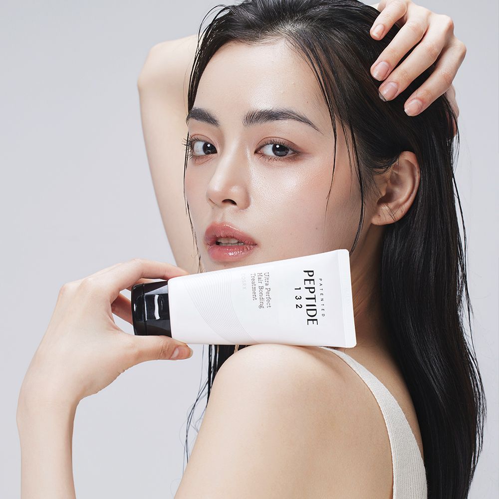Een vrouw houdt een witte tube vast met opschrift PEPTIDE 132 Ultra Perfect Hair Bonding Treatment.