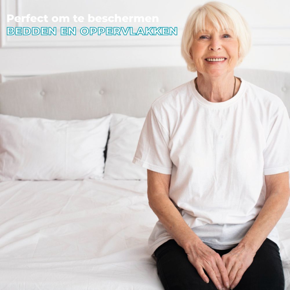 Oudere vrouw zit op een bed. Op de achtergrond een bed met wit beddengoed.