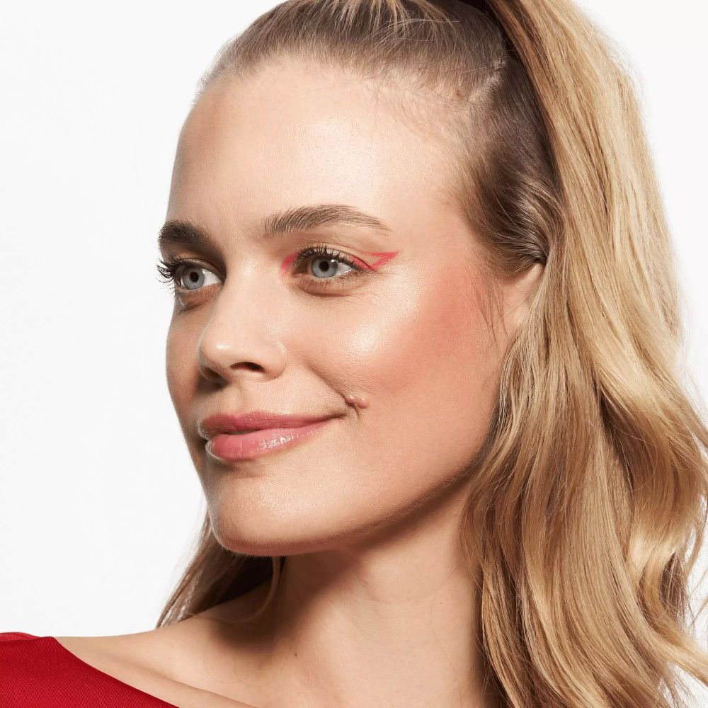 Portrait d'une femme avec du baume à lèvres rose. Cheveux blonds, eye-liner rouge.