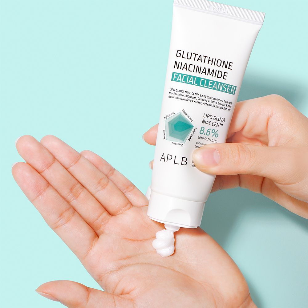 Main pressant un tube blanc, nettoyant visage dispensé dans la paume. Contient 8,6% Lipo Gluta Niac Cen.